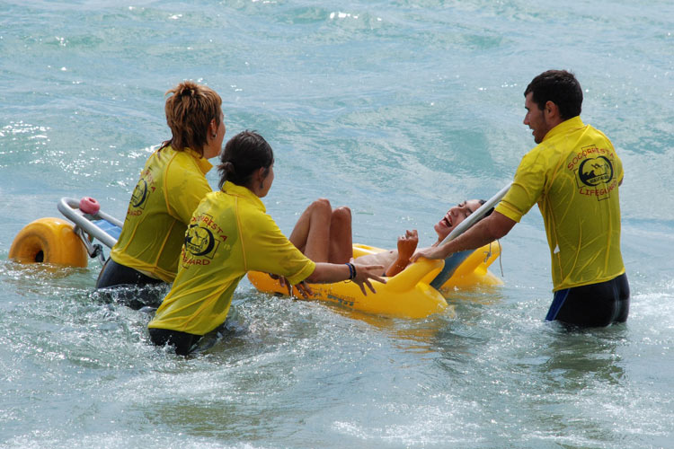 Uns monitors ajuden un jove discapacitat a banyar-se, a la platja de Torre Valentina.
