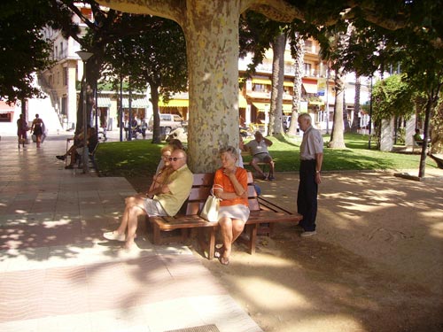 Un grup de gent gran, asseguts a l'ombra al passeig del Mar de Palamós.