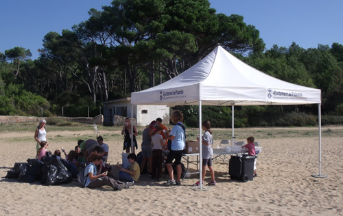 La carpa muntada ahir a la platja de Castell i algunes de les bosses de deixalles.