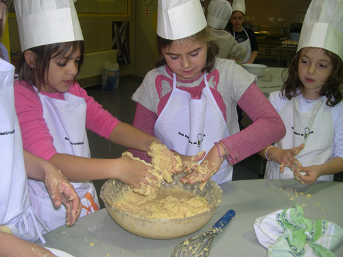 Tres nenes preparen una massa en el taller de l'Aula Gastronòmica.
