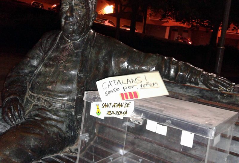 Una urna i missatges a favor del referèndum al costat de l'estàtua de mossèn Gumersind, a Sant Joan. (Foto: Rafel Bonillo).