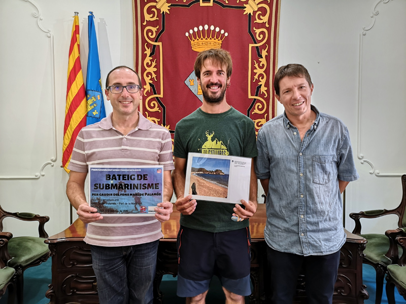 Pau Fernández, guanyador del concurs, entre l'alcalde Lluís Puig i el regidor Xavier Lloveras. (Foto: Ajuntament de Palamós).