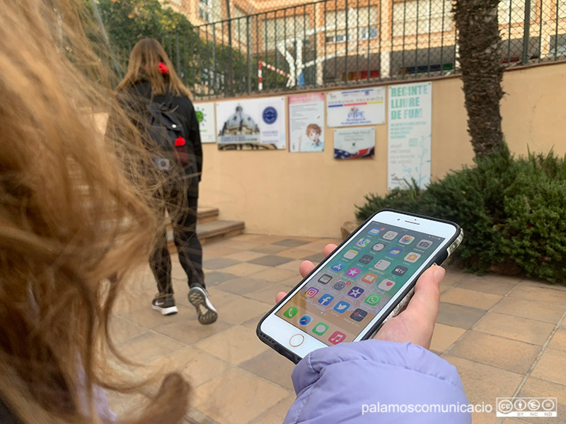 Una alumna amb el telèfon mòbil, abans d'entrar a l'escola.